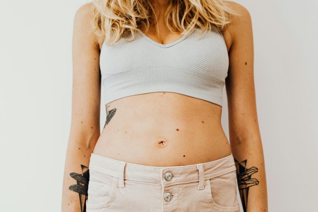 Close-up of a woman's midsection wearing a sports bra, showcasing tattoos and casual style.